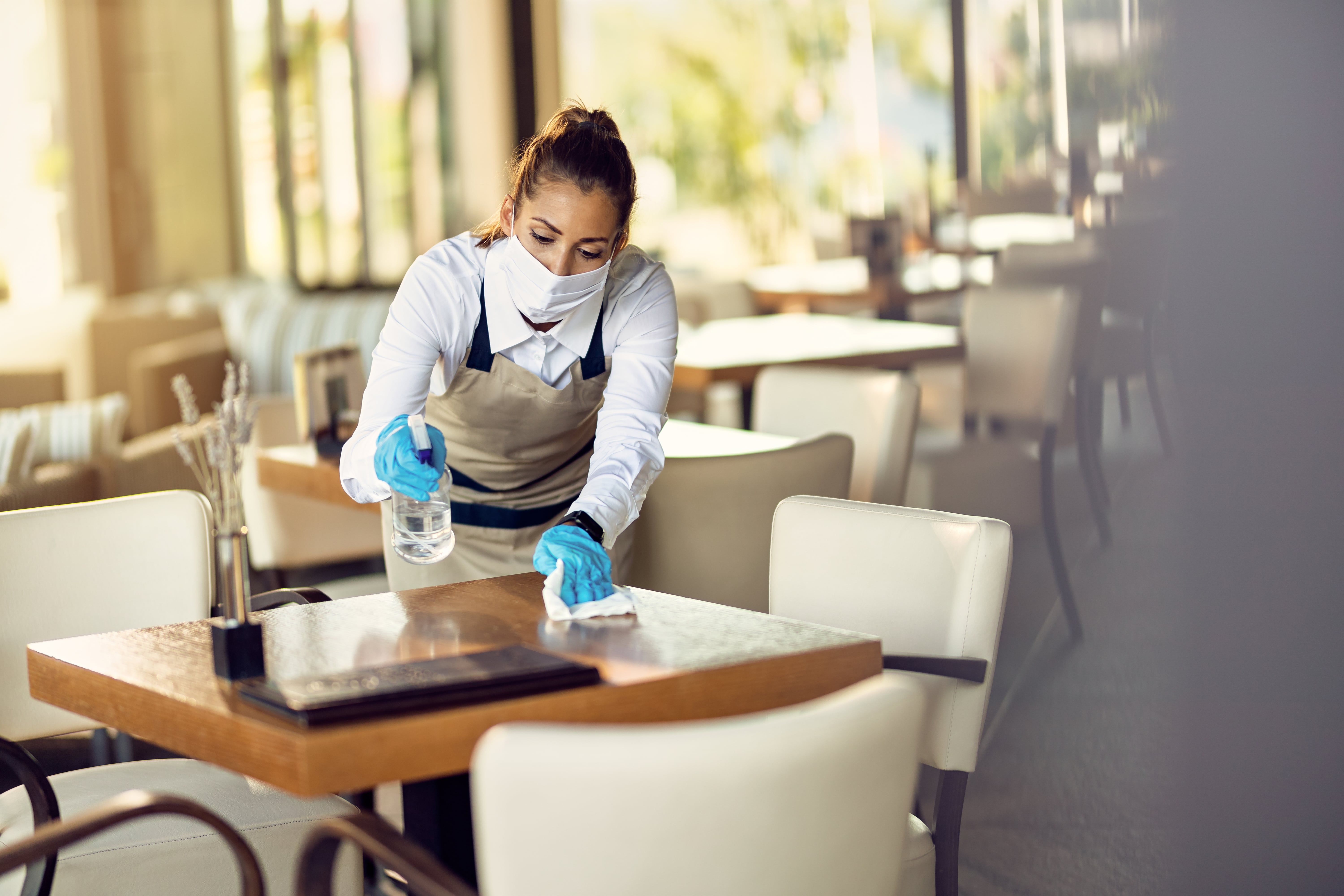 waitress with face mask disinfecting restaurant tables due coronavirus pandemic