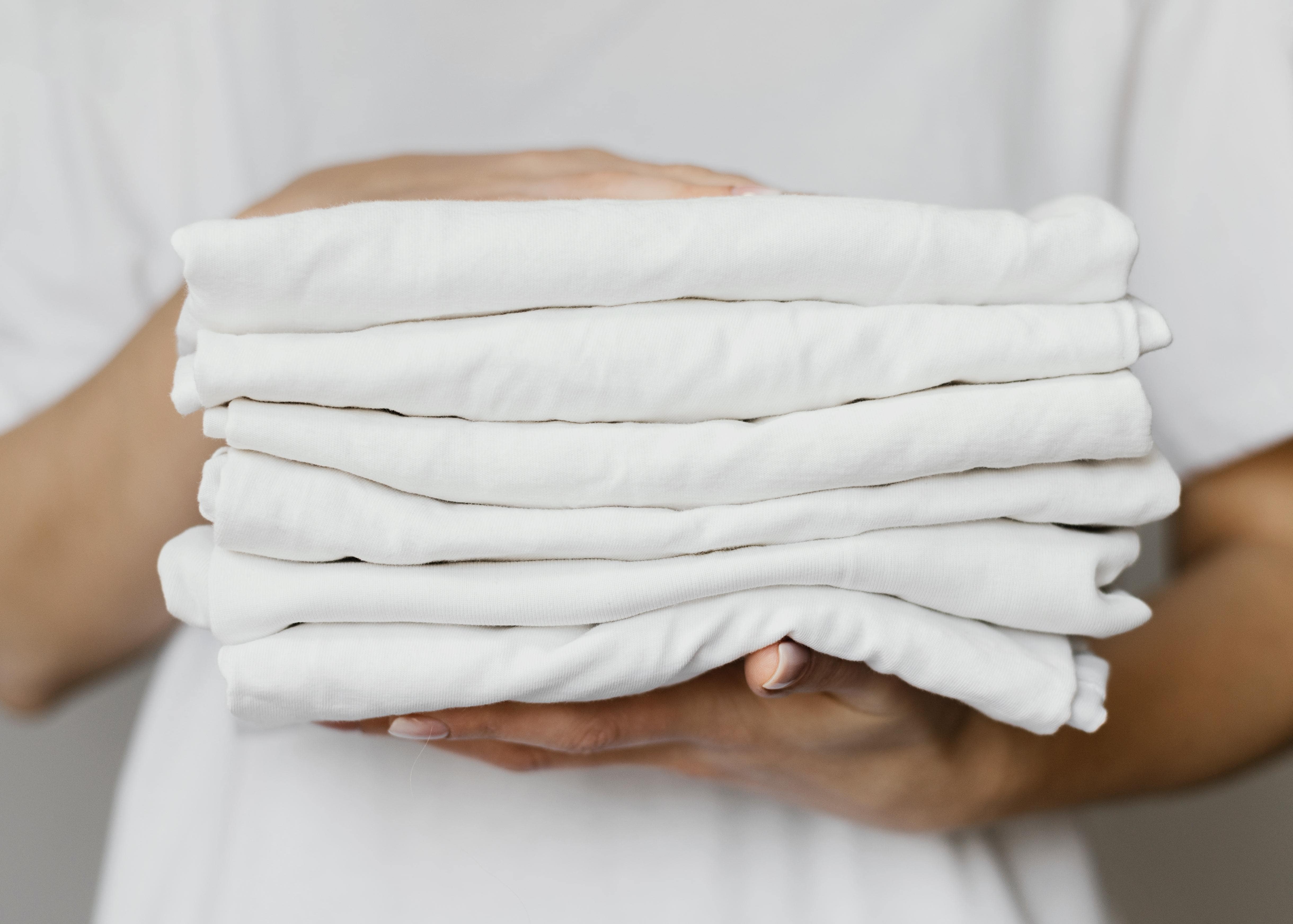 Hands holding a stack of clean, Crisply folded white clothes after washing at the correct water temperature