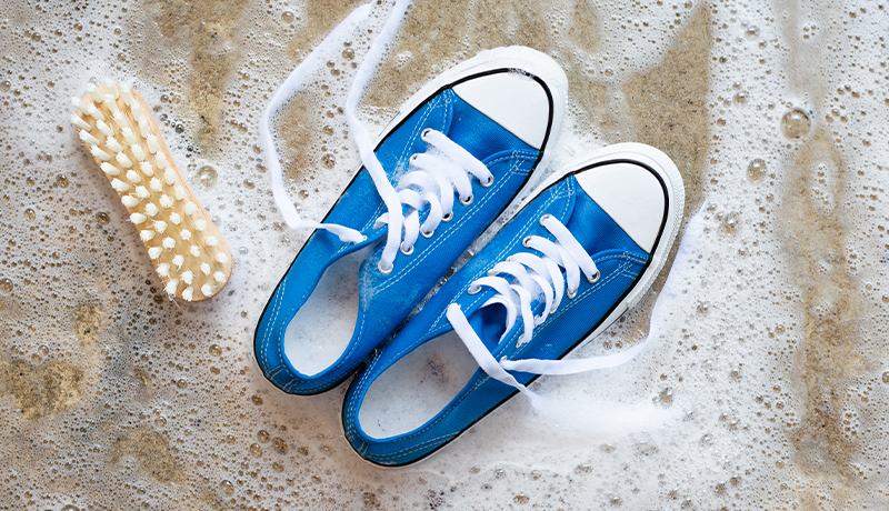 Blue Canvas Sneakers Soaking in Soapy Water with a Scrub Brush, Illustrating Shoe Cleaning Process