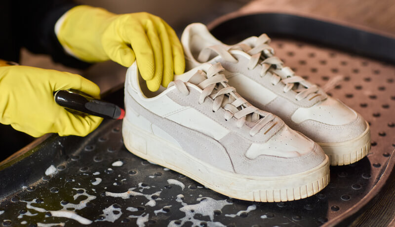 A professional shoe technician using a specialized brush and cleaning solution to deep clean white leather sneakers, highlighting the difference between DIY and professional results.