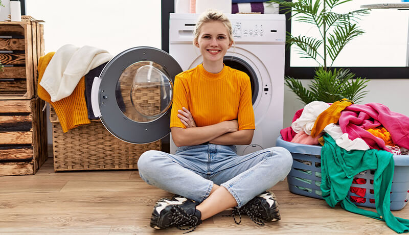 A woman struggling to pull a pink garment from an overflowing blue laundry basket, illustrating the common mistake of overloading that leads to inefficient cleaning and fabric damage.