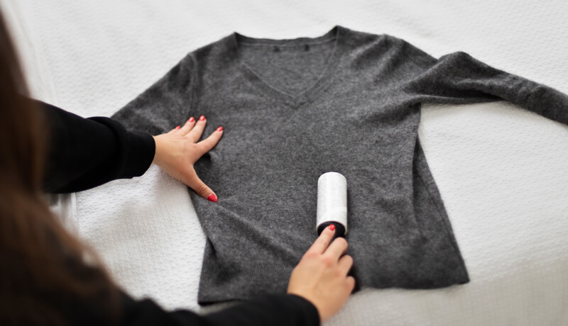 Close-up of a person's hands gently hand-washing a dark black velvet garment in a white basin with soapy water, demonstrating a technique to minimize the friction that causes fading.