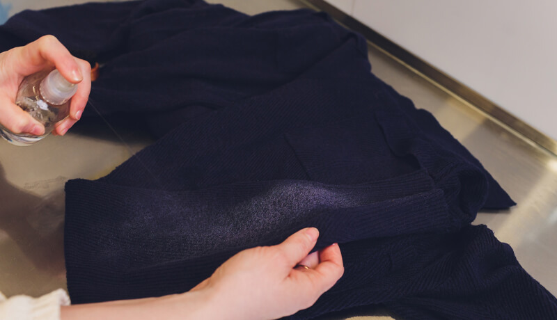 A professional staff member in a maroon apron presenting tall, uniform stacks of crisp white towels, illustrating the scale and consistency of a professional laundry service.