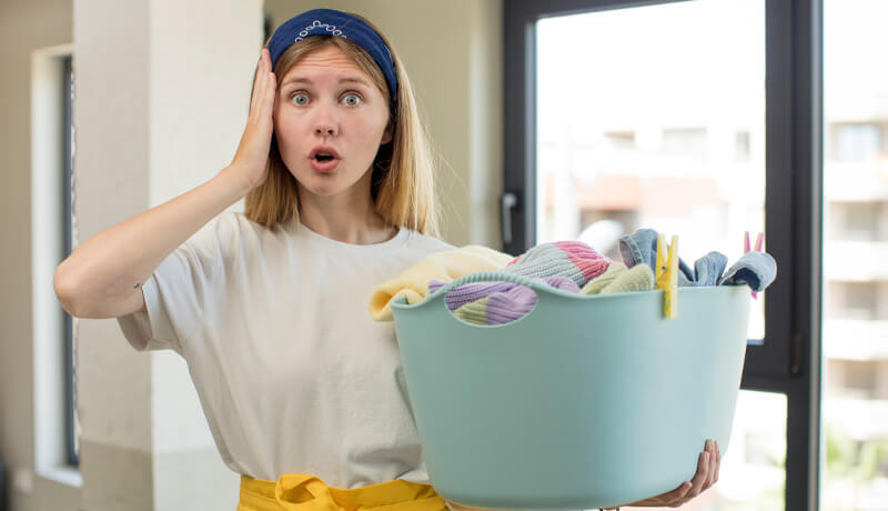 A bright blue laundry basket overflowing with an unsorted mix of vibrant pink, orange, and dark teal garments, highlighting how failing to separate colors leads to laundry day disasters.