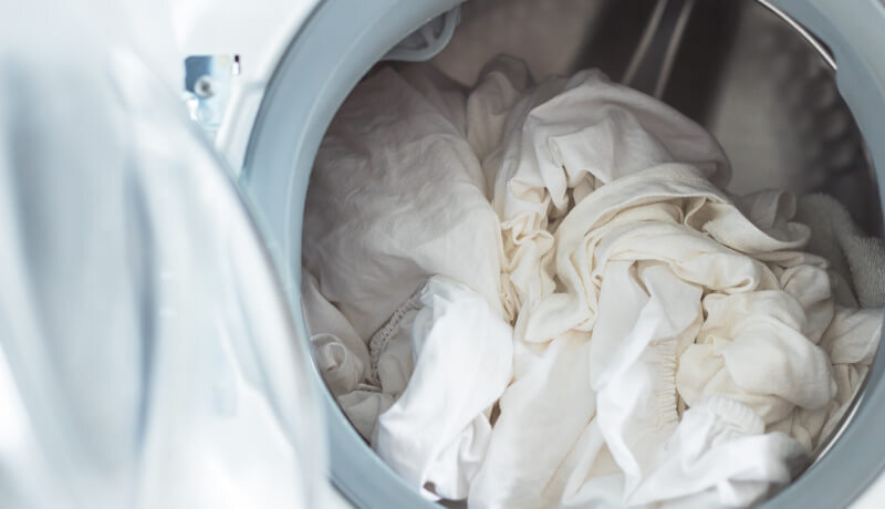 A man in a plaid shirt loading laundry into a large, industrial-grade stainless steel washing machine, showcasing the high-capacity equipment used at professional facilities.