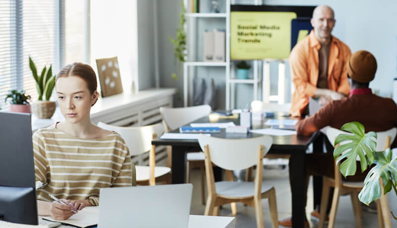 A young professional woman in a striped shirt working intently at her desk in a bright, modern open-plan office, illustrating the high level of focus achieved in a clean and well-managed workspace.